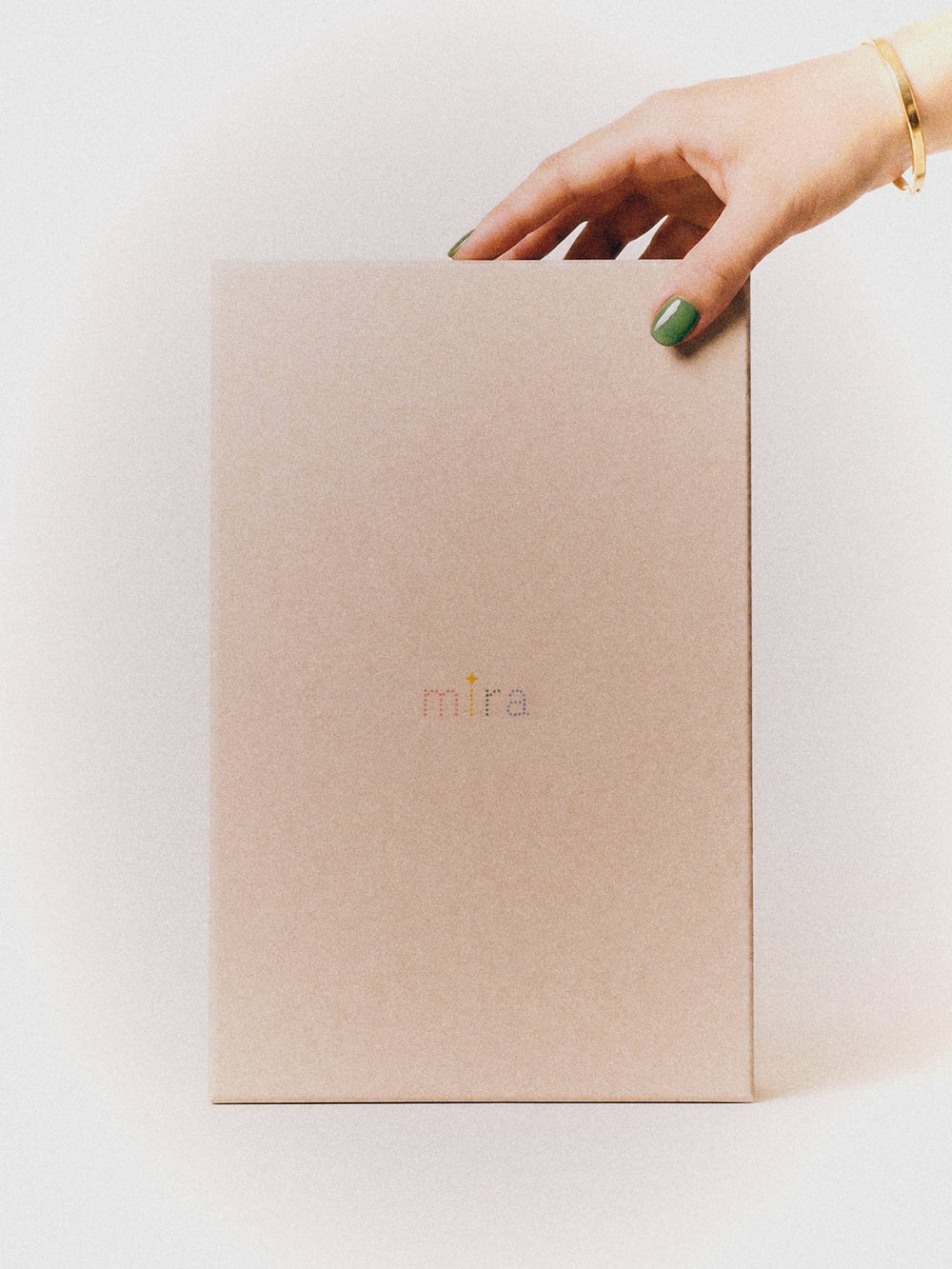 The Mira Box, closed, held in one hand against a soft grey ground