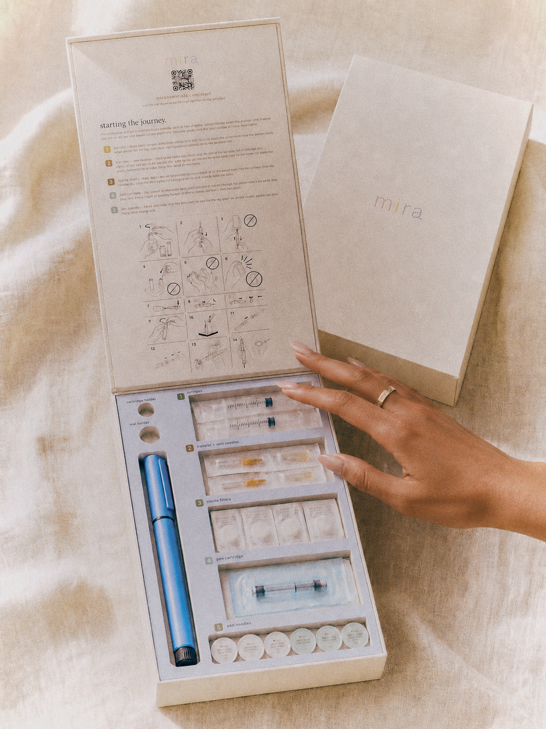 The Mira Box open on linen, the illustrated walkthrough inside the lid and the numbered tray of sterile sundries